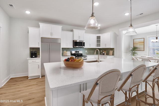 kitchen featuring visible vents, a sink, tasteful backsplash, stainless steel appliances, and light wood finished floors