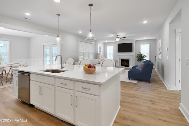 kitchen featuring visible vents, a sink, a lit fireplace, light wood finished floors, and dishwasher