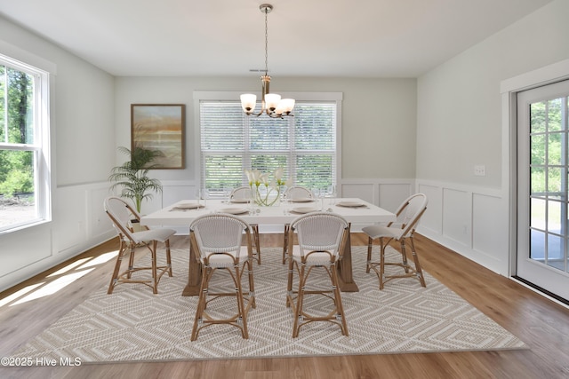 dining room with a notable chandelier, a decorative wall, a wainscoted wall, and wood finished floors