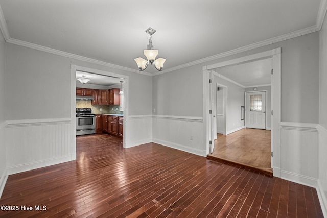 unfurnished dining area featuring dark wood-type flooring, an inviting chandelier, ornamental molding, and wainscoting