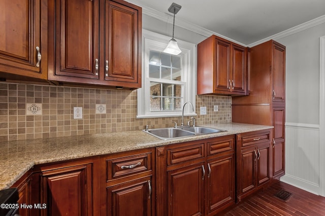 kitchen featuring dark wood-style floors, ornamental molding, hanging light fixtures, a sink, and wainscoting