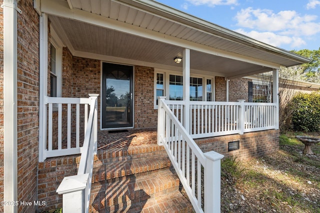 view of exterior entry featuring brick siding and covered porch