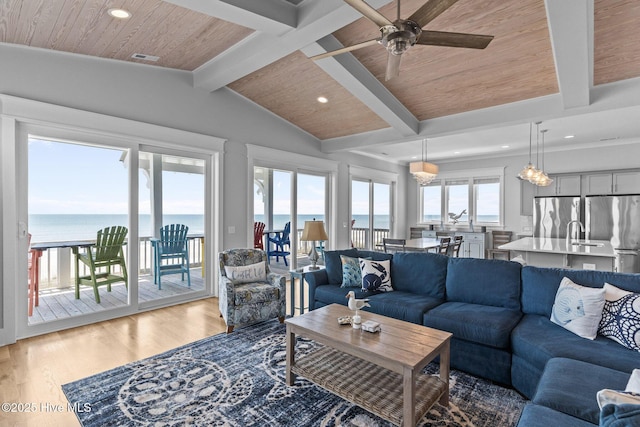 living area with vaulted ceiling with beams, light wood finished floors, a water view, and wooden ceiling