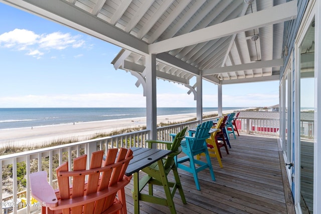 wooden terrace with a water view, outdoor dining space, and a view of the beach
