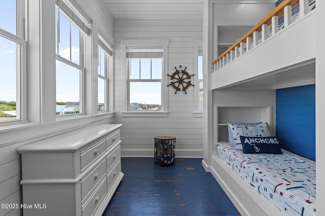 bedroom with baseboards, wood walls, and multiple windows