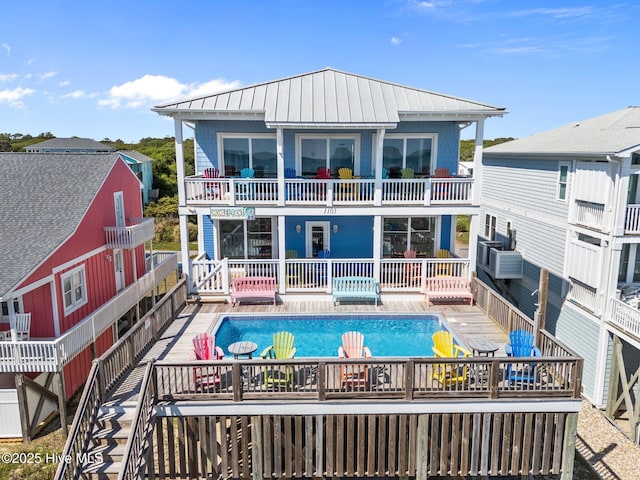 back of house with a standing seam roof, metal roof, and an outdoor pool