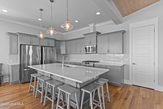 kitchen with gray cabinetry, a breakfast bar, stainless steel appliances, and a sink