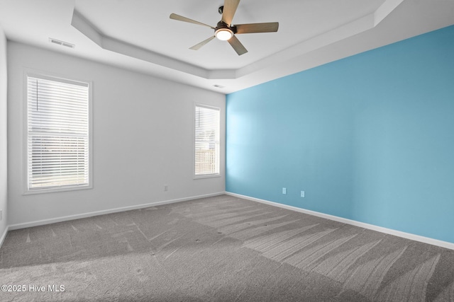 carpeted spare room featuring a tray ceiling, baseboards, visible vents, and ceiling fan