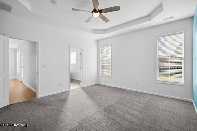 carpeted empty room featuring a tray ceiling, baseboards, visible vents, and ceiling fan