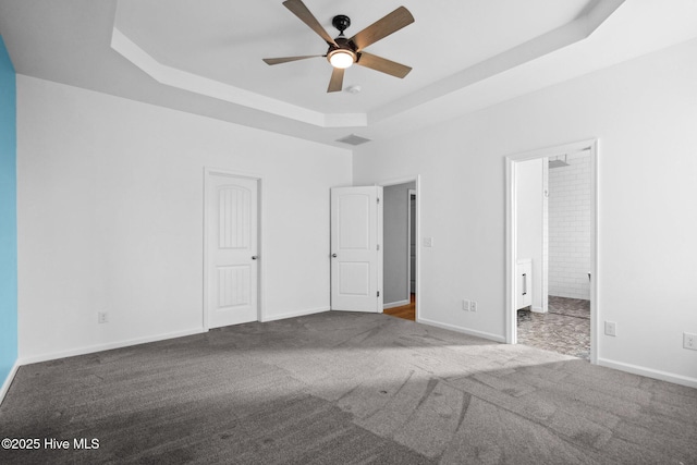 unfurnished bedroom with visible vents, baseboards, ensuite bath, a tray ceiling, and carpet flooring