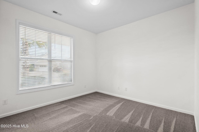 unfurnished room with visible vents, dark carpet, and baseboards