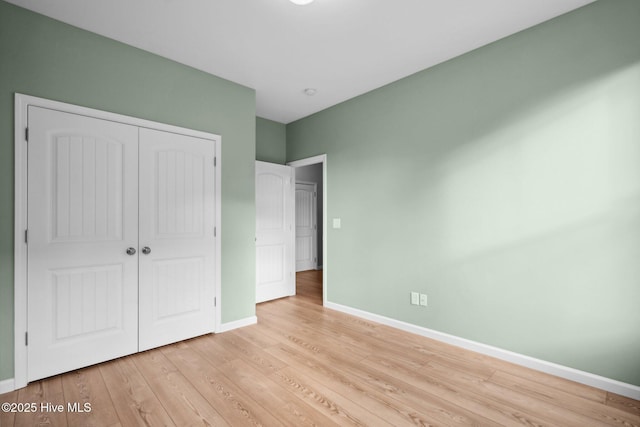 unfurnished bedroom featuring light wood finished floors, a closet, and baseboards