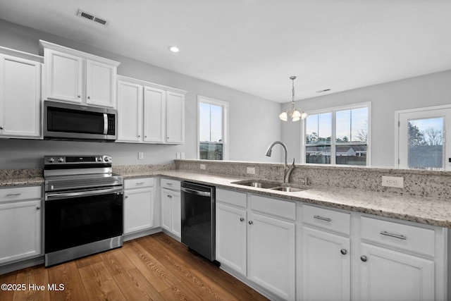 kitchen featuring visible vents, appliances with stainless steel finishes, wood finished floors, white cabinets, and a sink