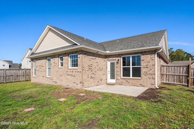 rear view of house featuring roof with shingles, brick siding, a fenced backyard, a patio area, and a lawn