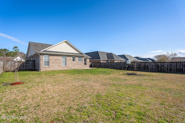 rear view of house featuring a fenced backyard, brick siding, and a yard