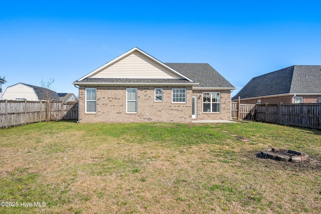 rear view of property featuring a yard, a fenced backyard, brick siding, and an outdoor fire pit