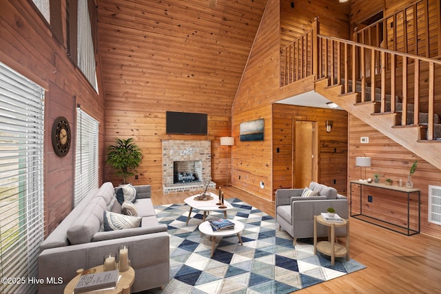 living area with wooden walls, stairs, an outdoor fireplace, a towering ceiling, and wood finished floors