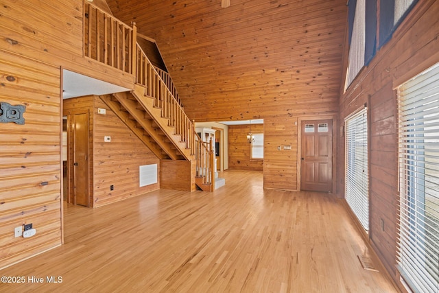 interior space with stairway, visible vents, light wood-style floors, a towering ceiling, and wood walls