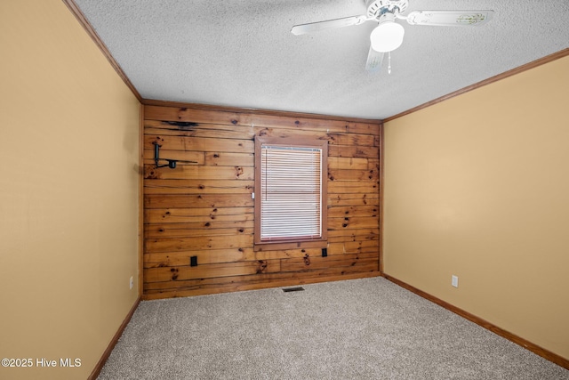 carpeted empty room with ornamental molding, visible vents, wood walls, and a textured ceiling