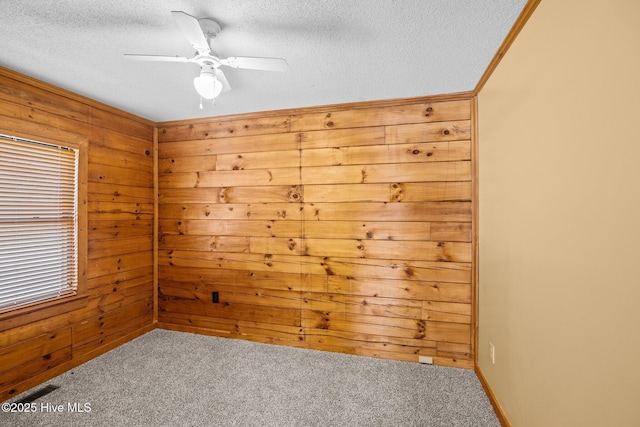 carpeted spare room featuring visible vents, a textured ceiling, ceiling fan, and wooden walls