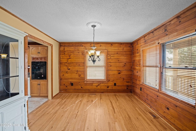 unfurnished dining area with light wood-style floors, visible vents, wood walls, and a chandelier