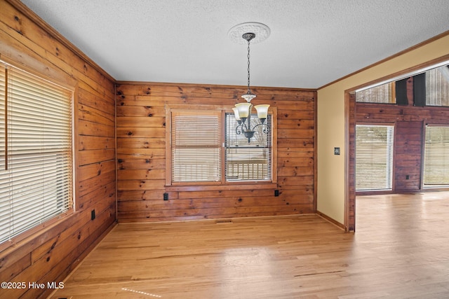 unfurnished dining area with wood walls, a textured ceiling, light wood-type flooring, and ornamental molding