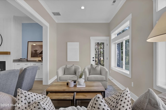 living area with light wood-type flooring, baseboards, visible vents, and crown molding