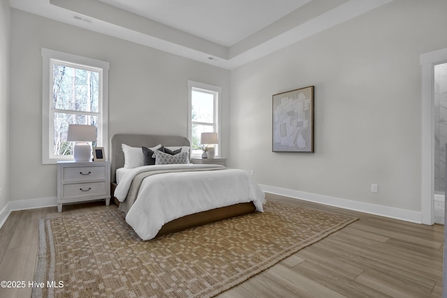 bedroom with visible vents, a tray ceiling, baseboards, and wood finished floors