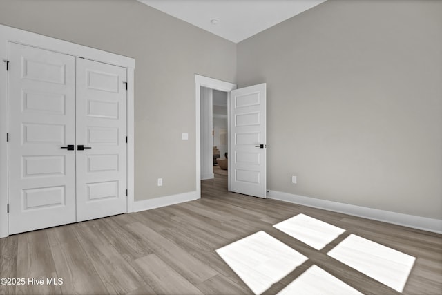 unfurnished bedroom featuring wood finished floors, baseboards, and a closet