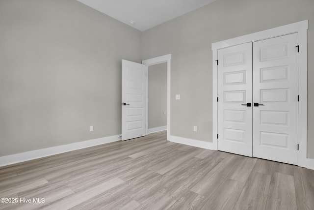 unfurnished bedroom featuring light wood-type flooring, a closet, and baseboards