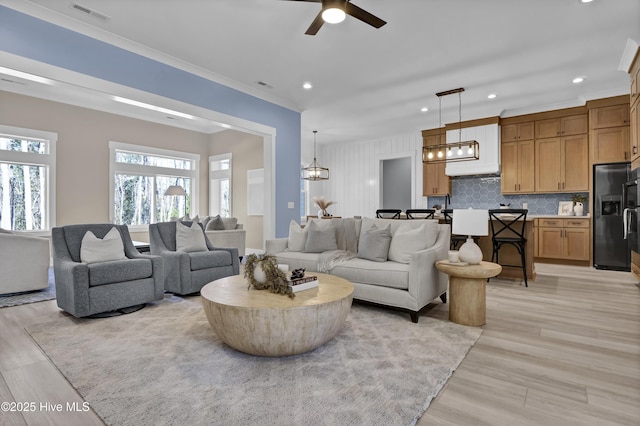 living room with visible vents, recessed lighting, crown molding, and light wood-style floors