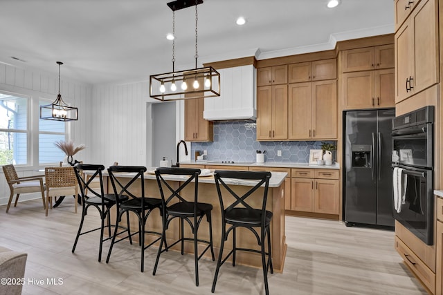 kitchen featuring pendant lighting, black appliances, an island with sink, a breakfast bar, and light countertops