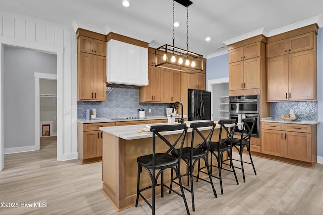 kitchen featuring black appliances, a center island with sink, a breakfast bar, decorative light fixtures, and light wood-style floors