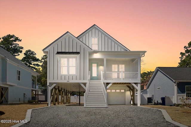 coastal inspired home featuring gravel driveway, a porch, stairway, and board and batten siding