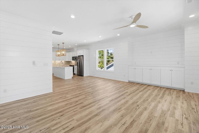 unfurnished living room with visible vents, ceiling fan with notable chandelier, light wood-type flooring, and a sink