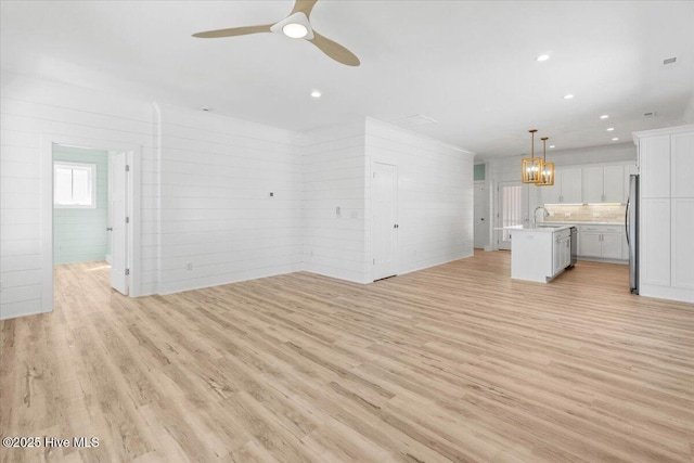 unfurnished living room with a sink, light wood-type flooring, recessed lighting, and ceiling fan with notable chandelier