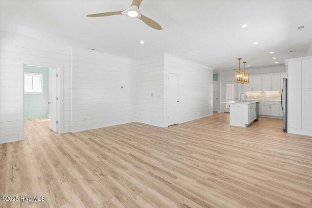 unfurnished living room with a sink, ceiling fan with notable chandelier, light wood-style floors, and recessed lighting