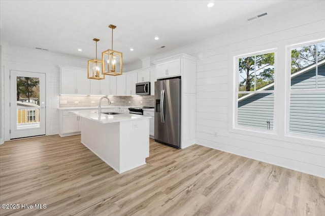 kitchen with light countertops, stainless steel appliances, a sink, light wood finished floors, and white cabinets