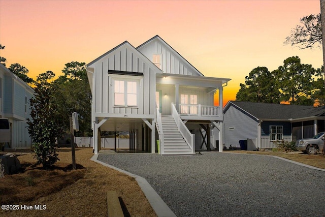 coastal inspired home with board and batten siding, gravel driveway, stairway, a porch, and a carport