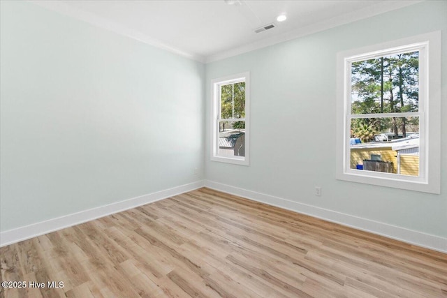 empty room featuring light wood-style floors, visible vents, crown molding, and baseboards