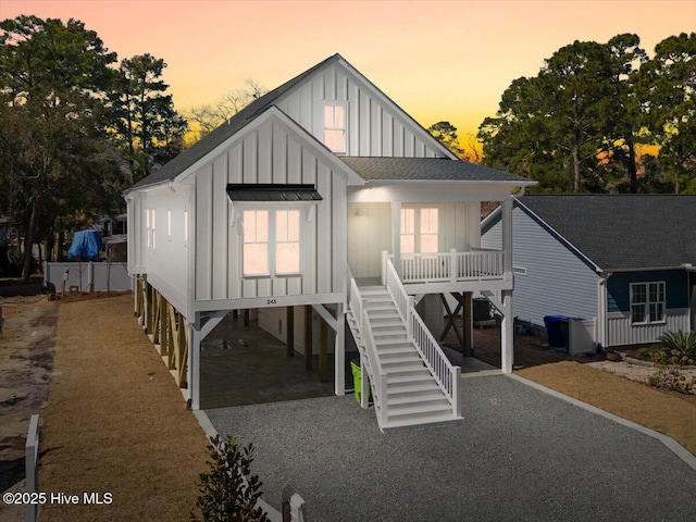 coastal inspired home featuring cooling unit, board and batten siding, a shingled roof, a carport, and stairs