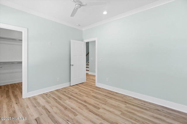 unfurnished bedroom featuring light wood-style flooring, crown molding, baseboards, ceiling fan, and a spacious closet