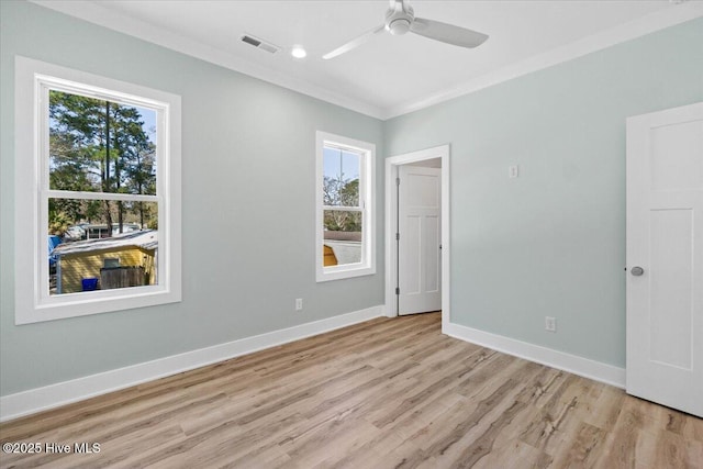 empty room with visible vents, ornamental molding, a ceiling fan, light wood-style floors, and baseboards