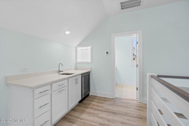 kitchen with lofted ceiling, a sink, beverage cooler, white cabinets, and visible vents