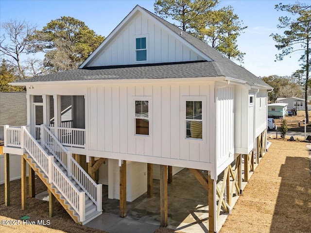 back of property featuring board and batten siding, roof with shingles, and stairs