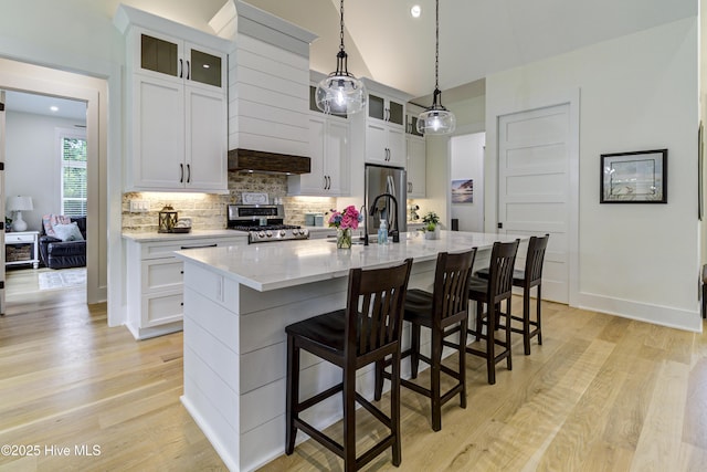 kitchen with an island with sink, range, light wood-style floors, and backsplash