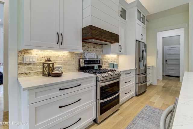 kitchen featuring backsplash, light wood-type flooring, custom range hood, appliances with stainless steel finishes, and white cabinets