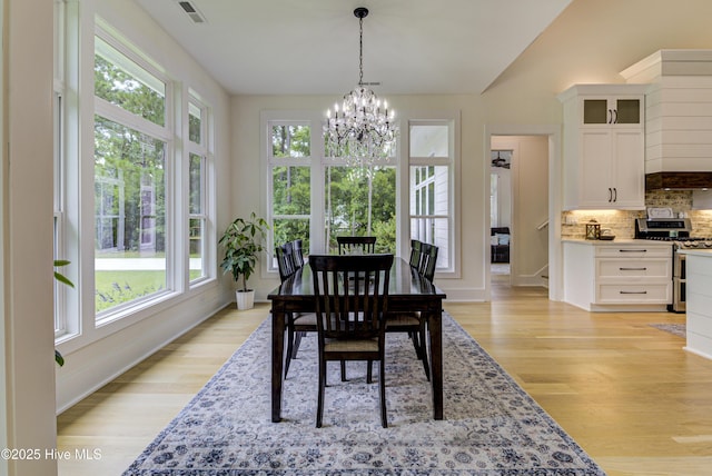 dining area with baseboards, visible vents, lofted ceiling, light wood-style flooring, and a notable chandelier