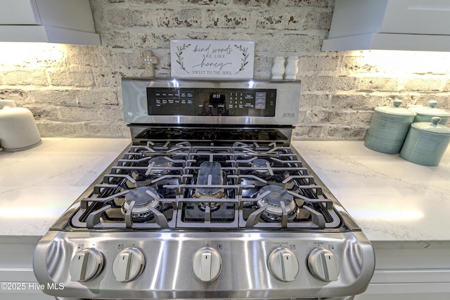 room details featuring stainless steel gas range oven, decorative backsplash, range hood, and light stone counters