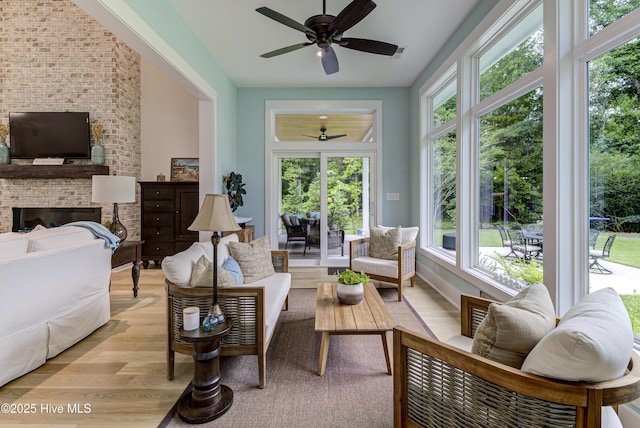 living area featuring a brick fireplace, light wood-type flooring, and ceiling fan